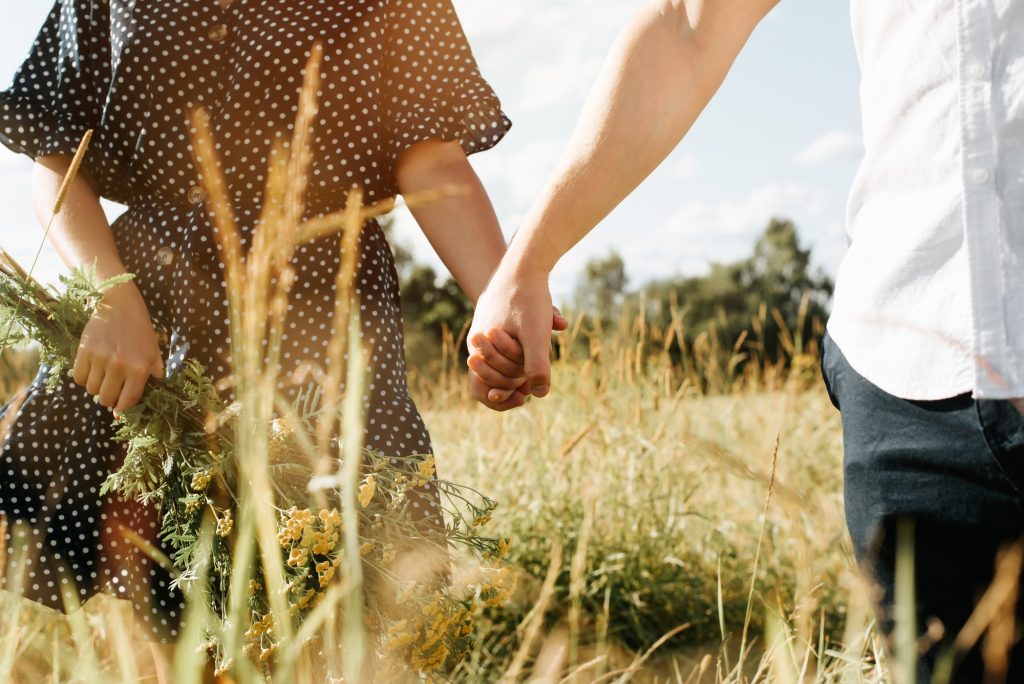 Close-up of young couple in love holding hands and walking in field on sunny summer day, enjoying